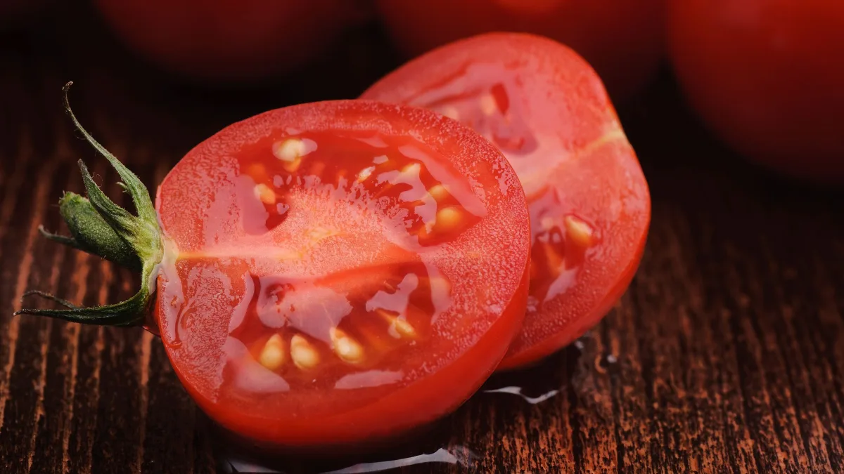 Tomates rouges entières et coupées en deux, graines visibles, sur un plan de travail en bois